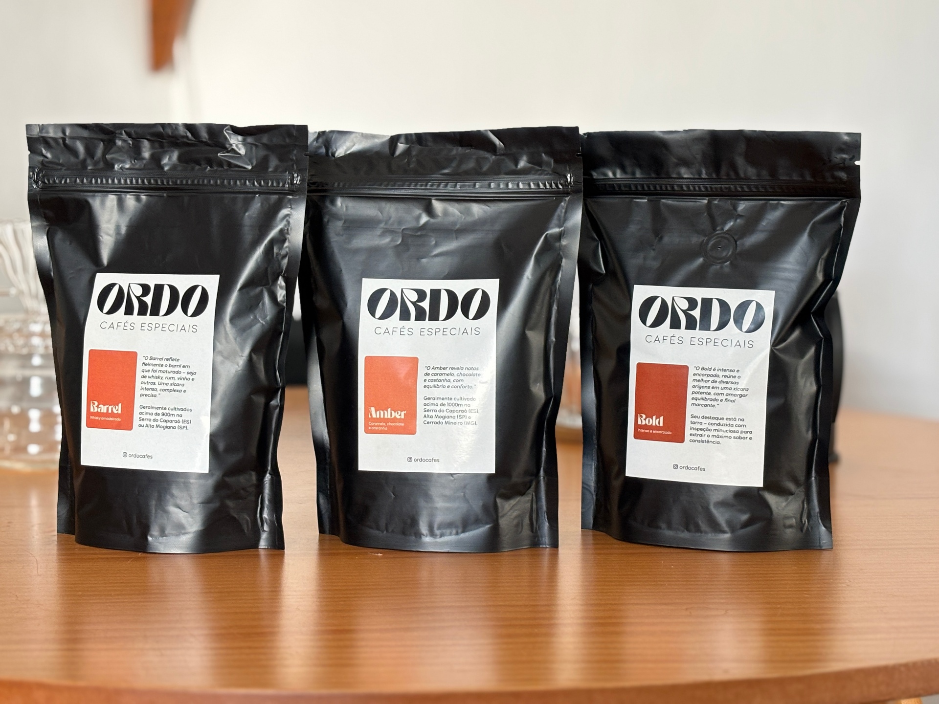 Embalagens dos cafés especiais Ordo: Barrel, Amber e Bold sobre mesa de madeira